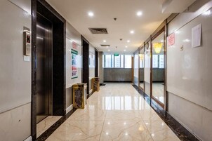 Un pasillo con piso de mármol, un ascensor y puertas de cristal que dan a las habitaciones.
