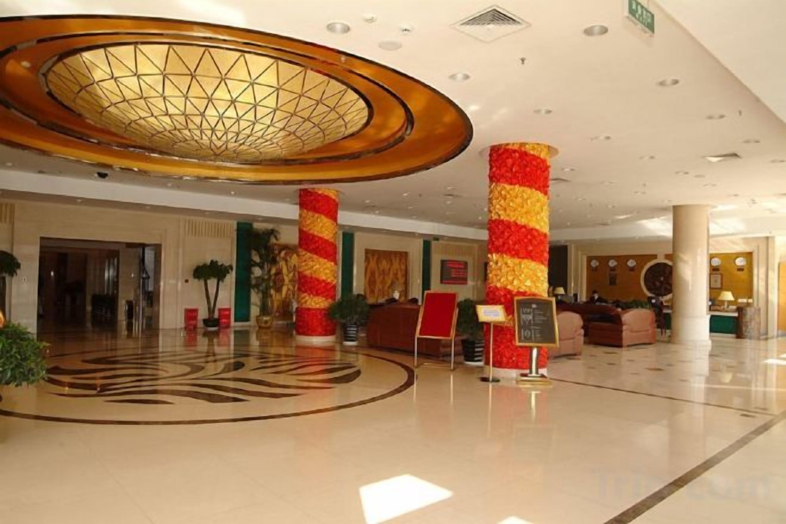 A hotel lobby with a large circular ceiling feature, a reception desk, and a seating area.