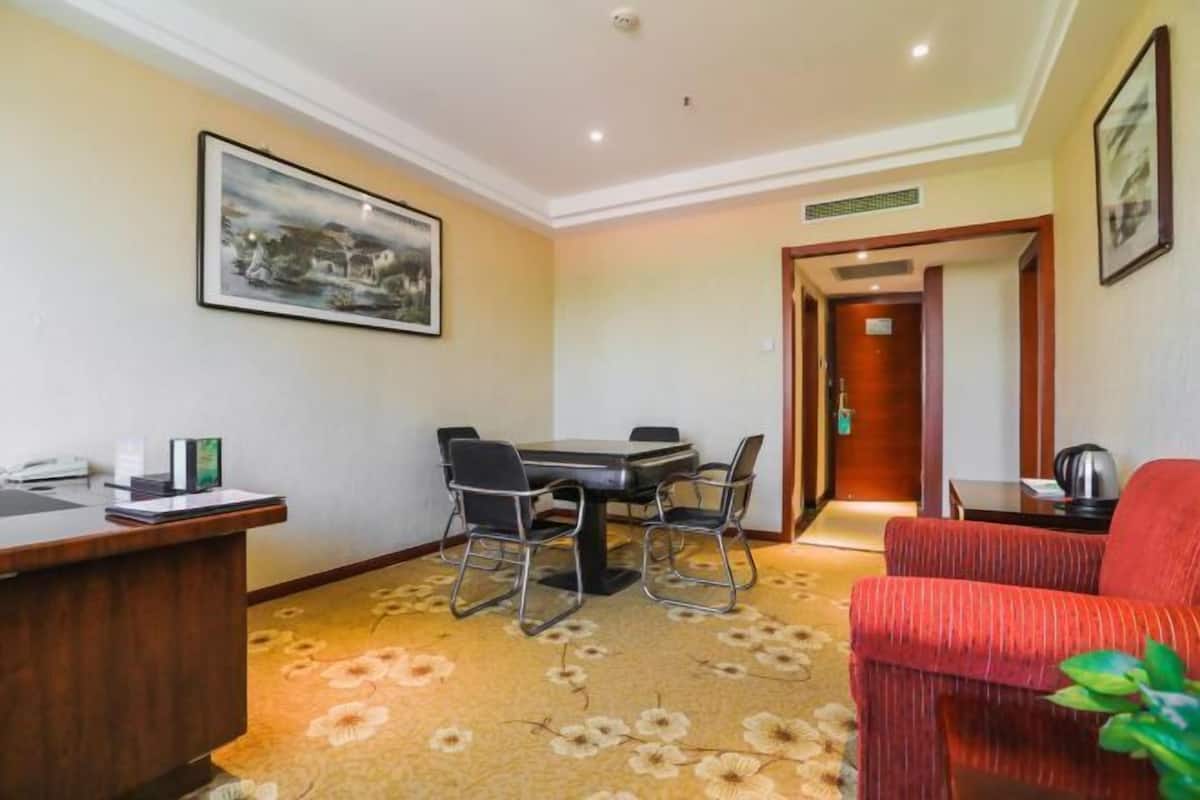 A hotel room with a dining table, chairs, a red sofa, a desk with a telephone, and a framed picture on the wall.