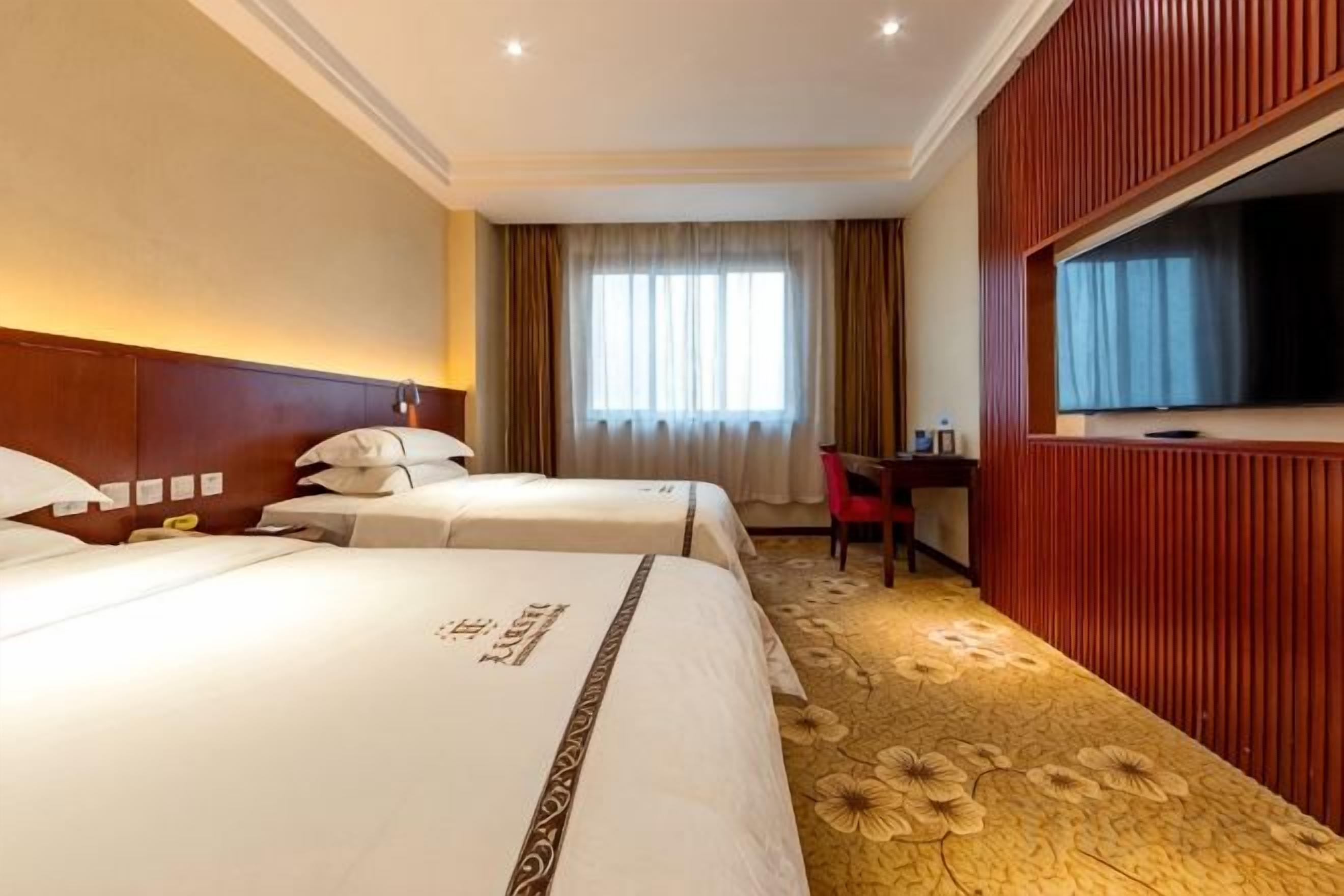 A hotel room with two beds, a desk, and a television.