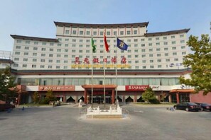 A large hotel building with multiple floors, a central entrance, and a flagpole with flags. - Haotian Holiday Hotel Beijing (Beijing)
