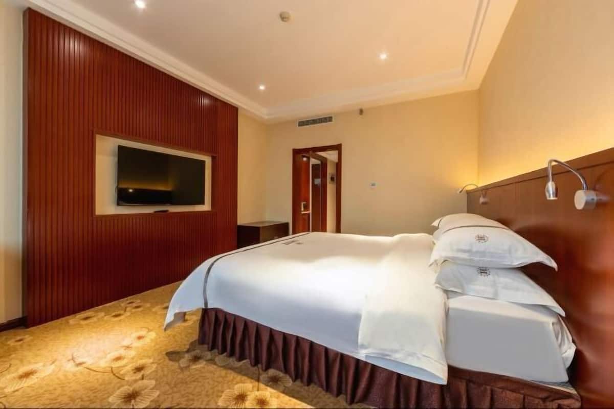 A hotel room with a large bed, a flat-screen TV mounted on the wall, and a wooden panel design on the walls.