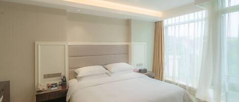 A modern hotel room with a large bed, a nightstand, a mirror, and a window with sheer curtains.
