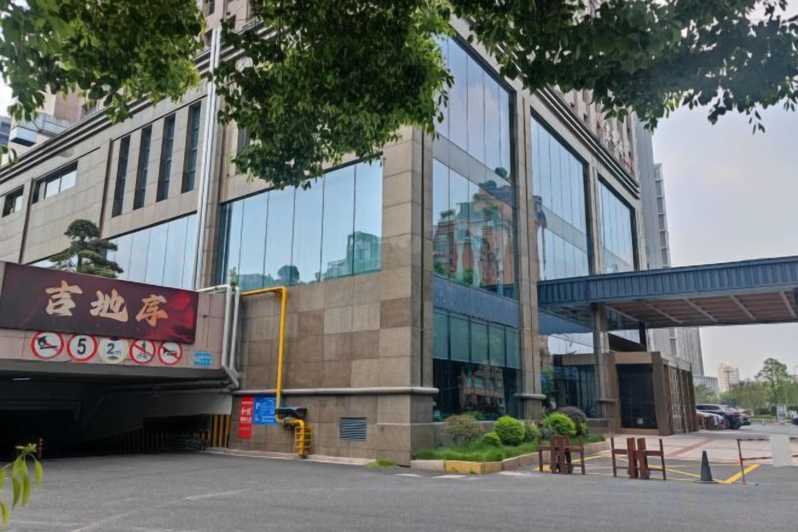 Een modern gebouw met een grote glazen gevel, een overdekte ingang en een parkeerplaats met duidelijke parkeerplaatsen.