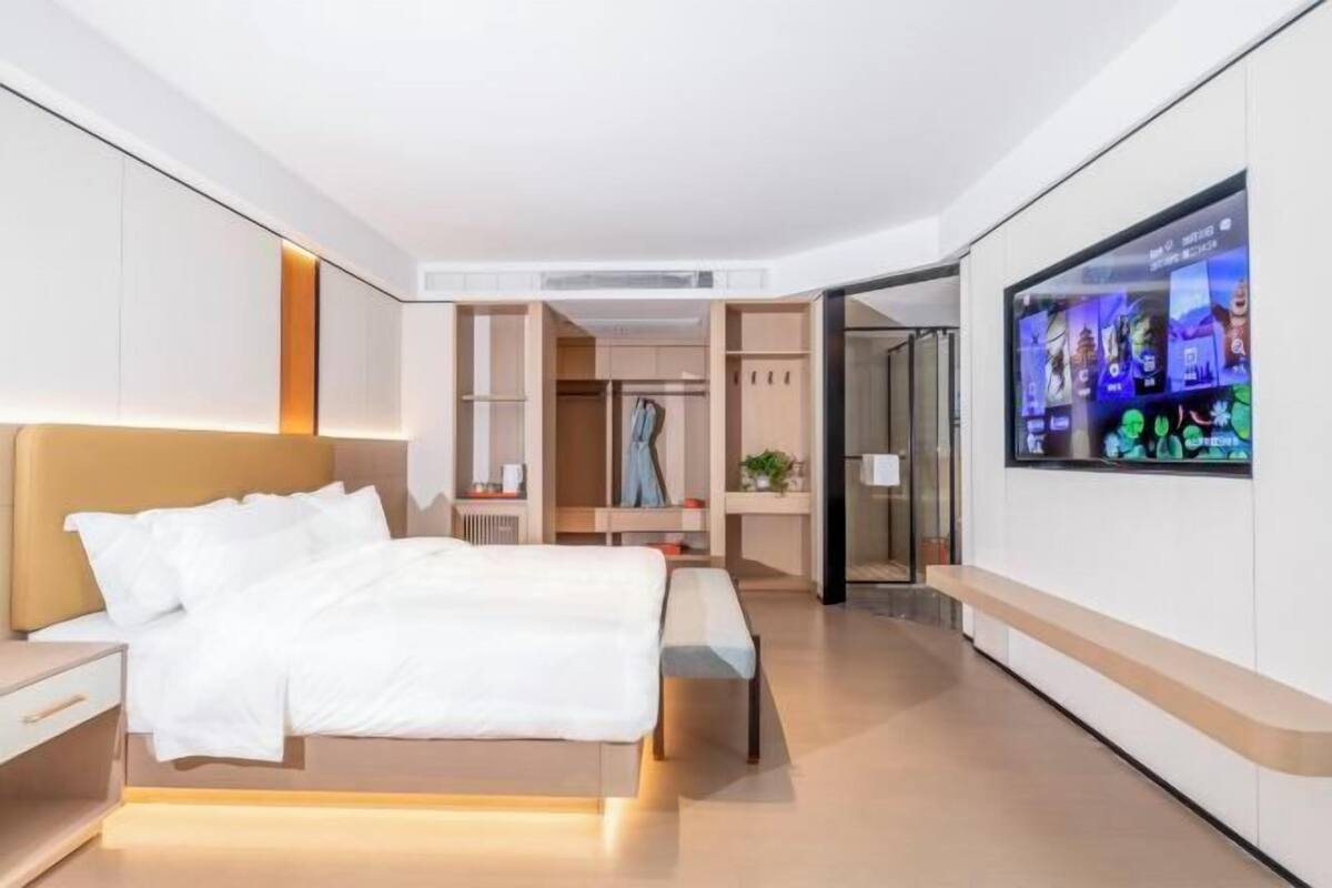 Une chambre d’hôtel moderne équipée d’un lit, d’une table de chevet, d’une télévision, d’une armoire et d’un banc.