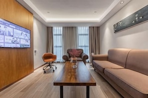 A modern living room with a wooden coffee table, a sofa, a chair, and a television mounted on the wall. - Hangzhou Junhu International Hotel (HANGZHOU)