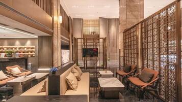 A spacious lobby with seating areas, a reception desk, and a television screen.