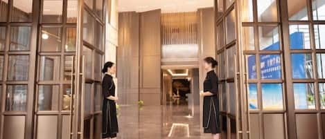 A hotel lobby with a glass partition, a reception desk, and a blue sign.
