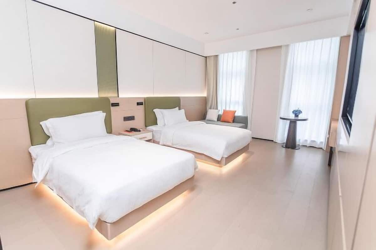 Une chambre d’hôtel avec deux lits, une petite table et une fenêtre avec des rideaux.