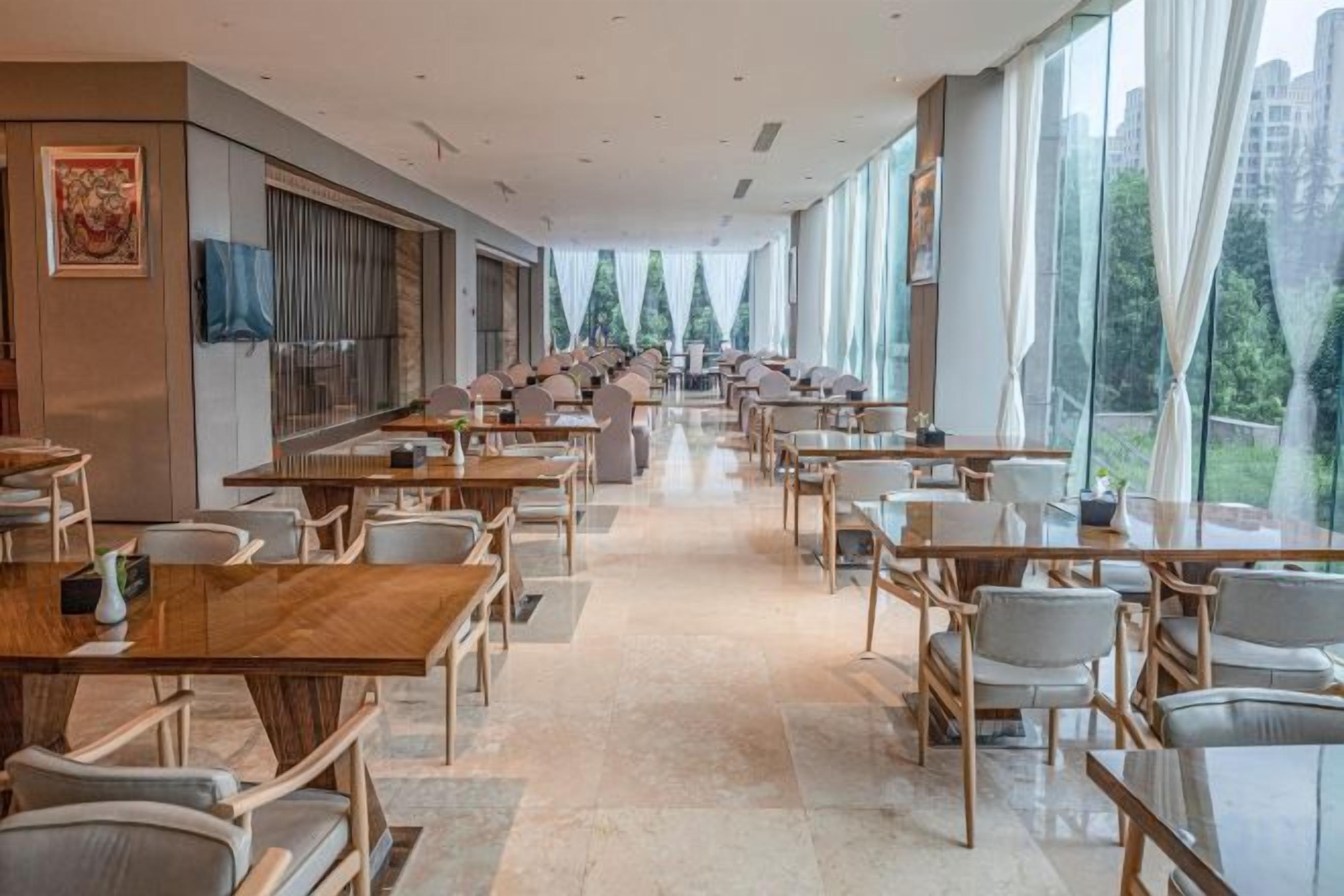A spacious dining area with long tables and chairs, large windows, and a modern interior design.