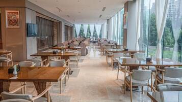 A spacious dining area with long tables and chairs, large windows, and a modern interior design.