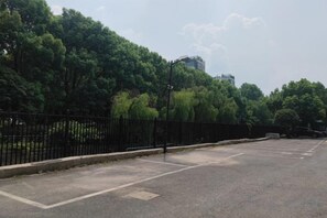A parking lot with a black fence, trees, and a building in the background. - Hangzhou Junhu International Hotel (HANGZHOU)