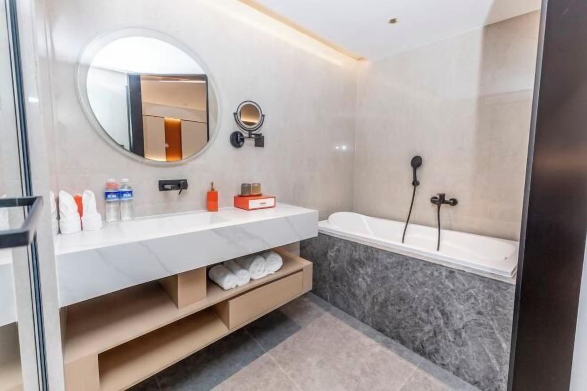 Une salle de bain moderne avec un meuble-lavabo blanc, un miroir rond, une baignoire et un espace douche.