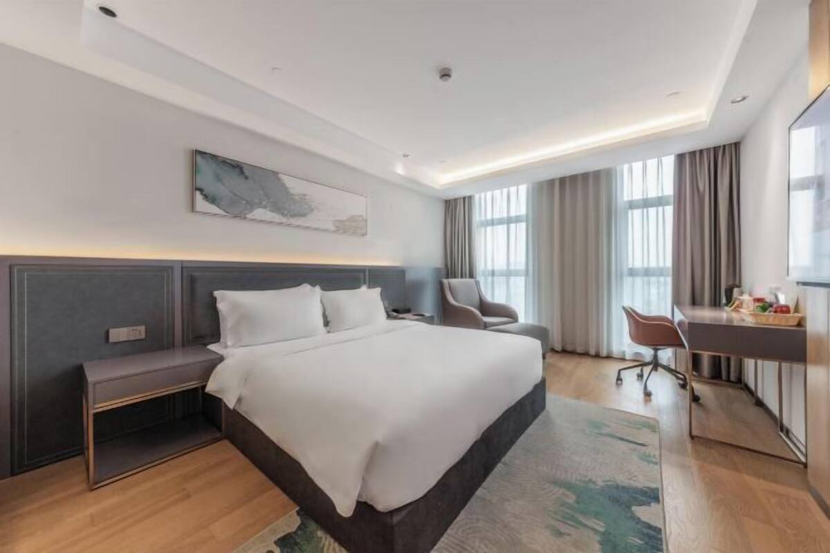 Une chambre d’hôtel moderne avec un grand lit, un bureau, une chaise et un tableau au mur.