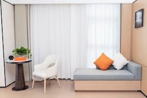 Une pièce moderne avec un canapé gris, une chaise blanche et une petite table ronde agrémentée d’une plante.