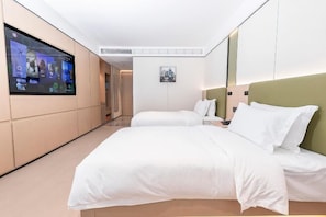 Une chambre d’hôtel dotée d’un grand téléviseur à écran plat fixé au mur, de deux lits avec une literie blanche, d’une petite table de chevet et d’un tableau encadré au mur.