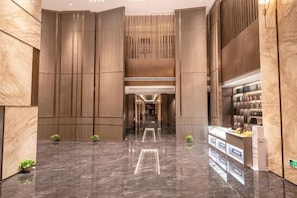 A modern hotel lobby with a marble floor, vertical wooden panels, and a reception desk.