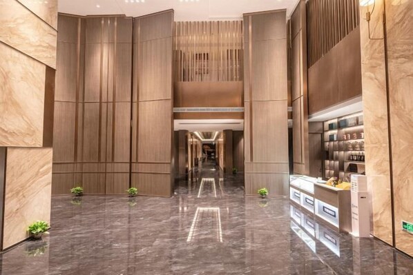 Een moderne hotelentree met een marmeren vloer, verticale houten panelen en een receptiebalie.
