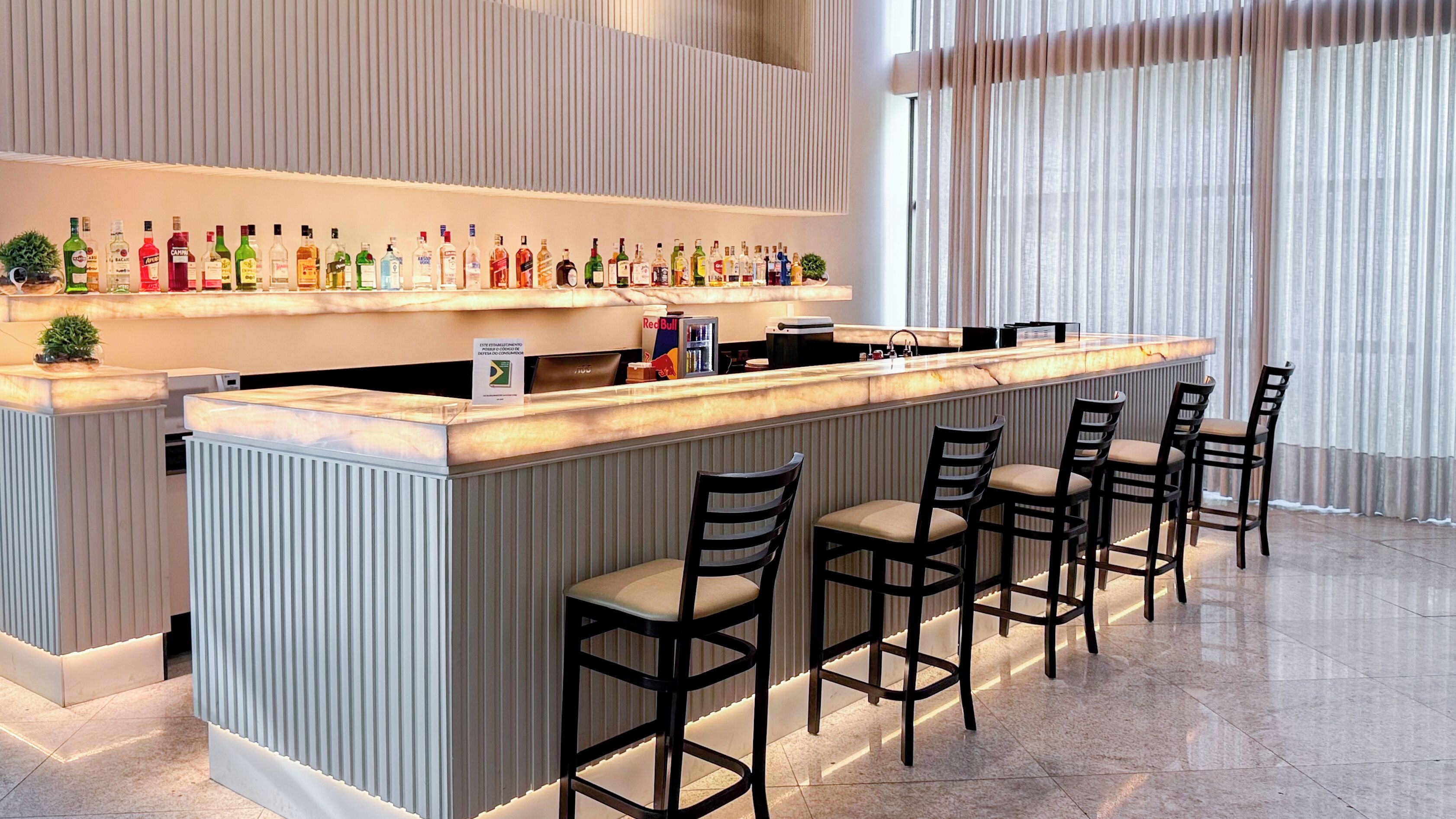 A bar area with a long counter and multiple stools, featuring a variety of liquor bottles.