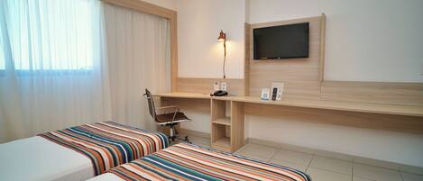 A hotel room with two beds, a desk, a chair, a TV, and a lamp.