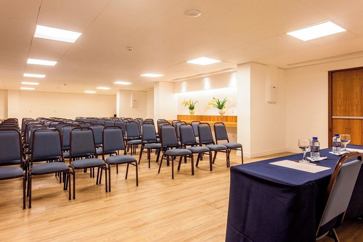 Un salón de conferencias con filas de sillas y una mesa con botellas de agua y vasos.