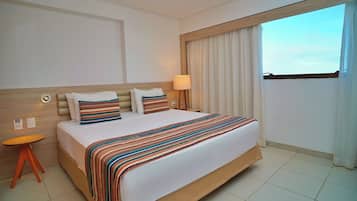 Habitación de hotel con una cama grande, una mesita de noche, una lámpara y vistas al cielo a través de la ventana.