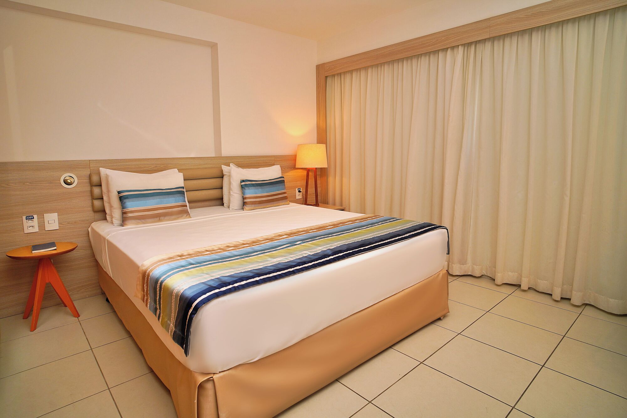A hotel room with a large bed, a bedside table, a lamp, and a window with curtains.