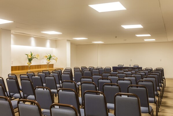 A conference room with rows of chairs, a podium, and two potted plants.