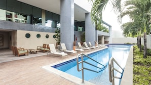 Una piscina con sillones de descanso y un área de cubierta con baldosas.