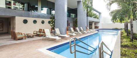 Una piscina con sillones de descanso y un área de cubierta con baldosas.