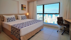 Habitación de hotel con una cama grande, un escritorio con silla, vistas a la ciudad y un cuadro en la pared.