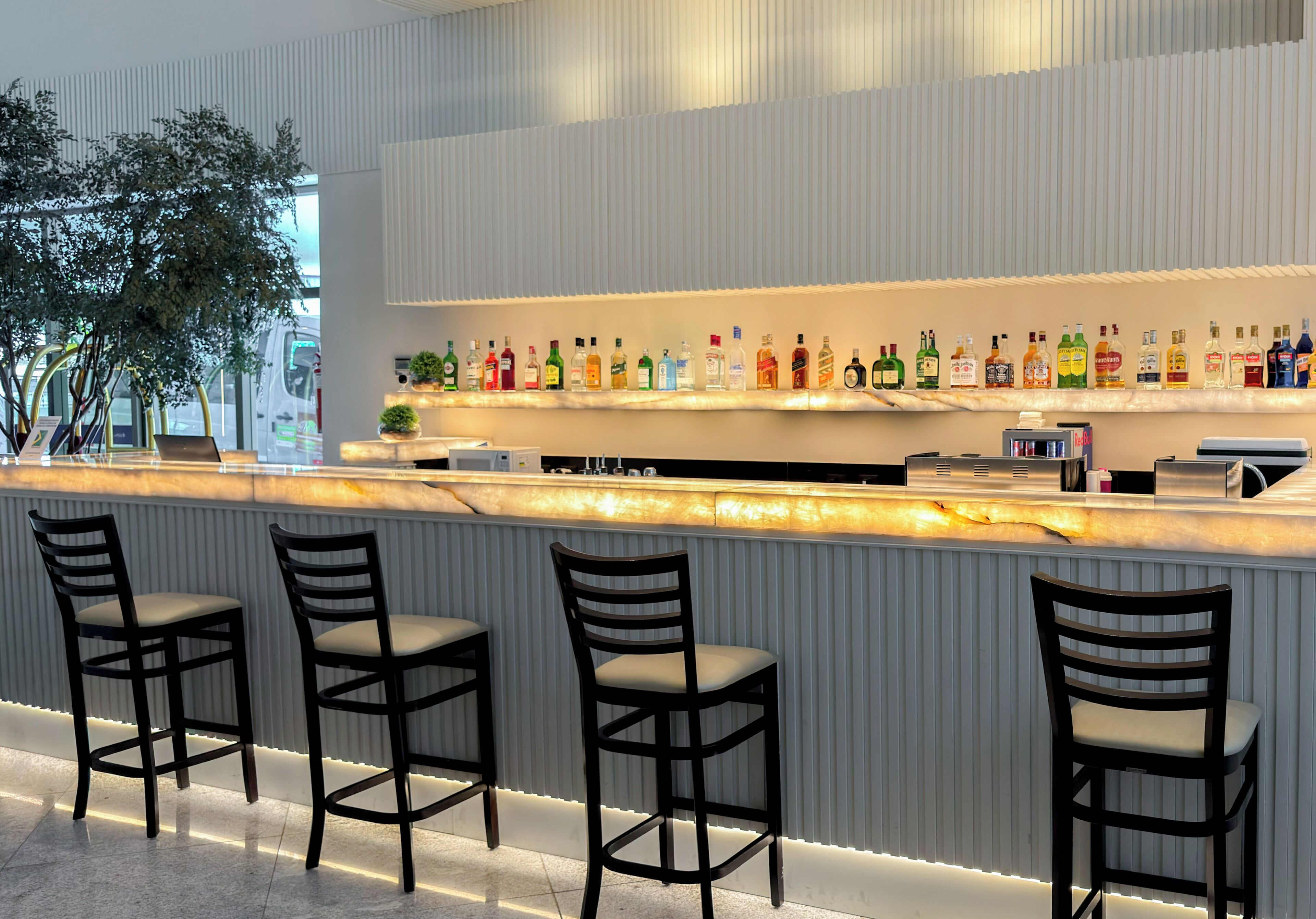 A bar area with a marble countertop, multiple liquor bottles, and three bar stools.