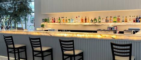 A bar area with a marble countertop, multiple liquor bottles, and three bar stools.