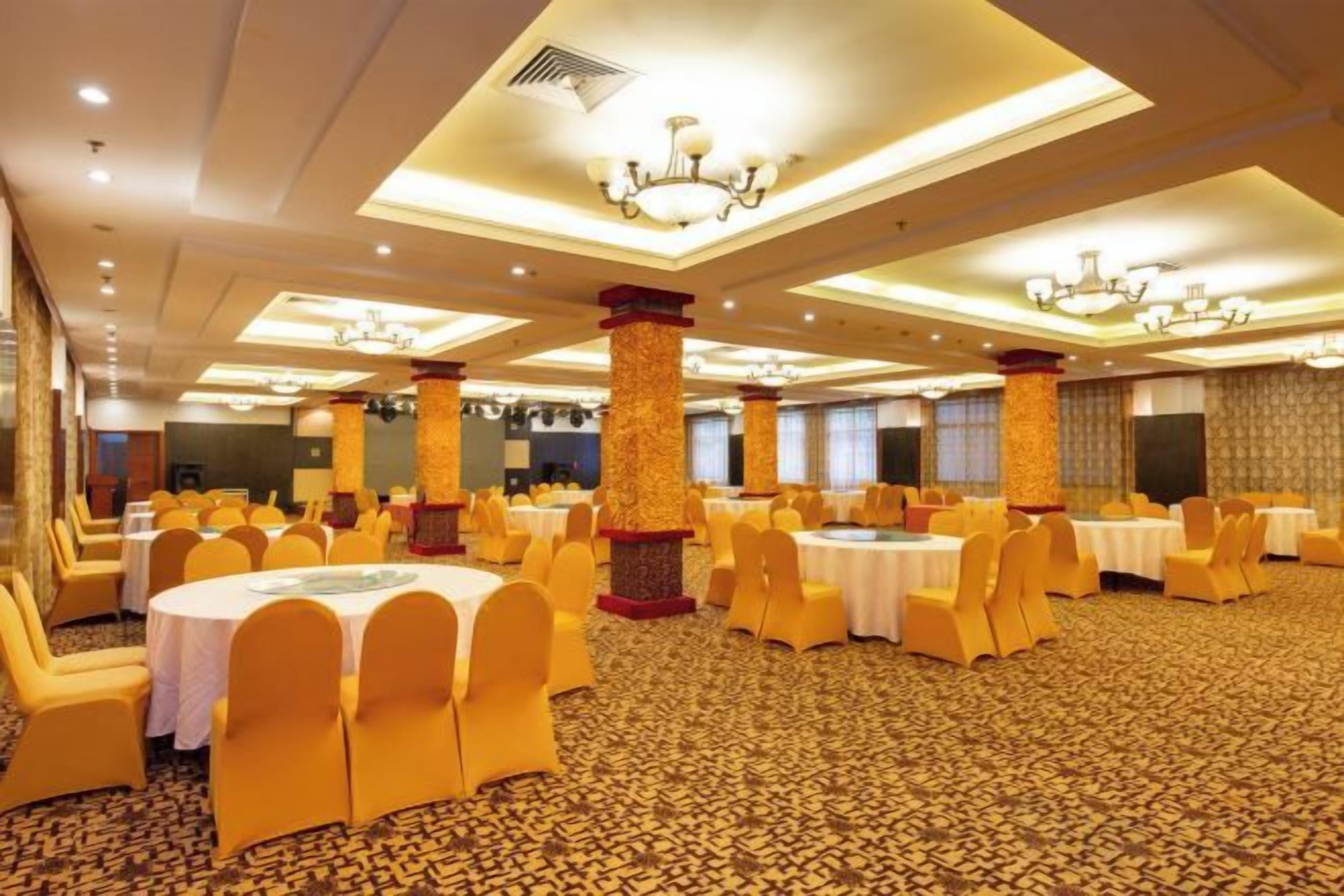 Un salón de banquetes con mesas y sillas redondas, techos altos con candelabros y suelo cubierto de alfombra estampada.