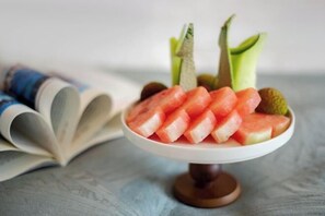 A bowl of watermelon and kiwi slices on a white plate, with a book and a rolled-up magazine in the background.
