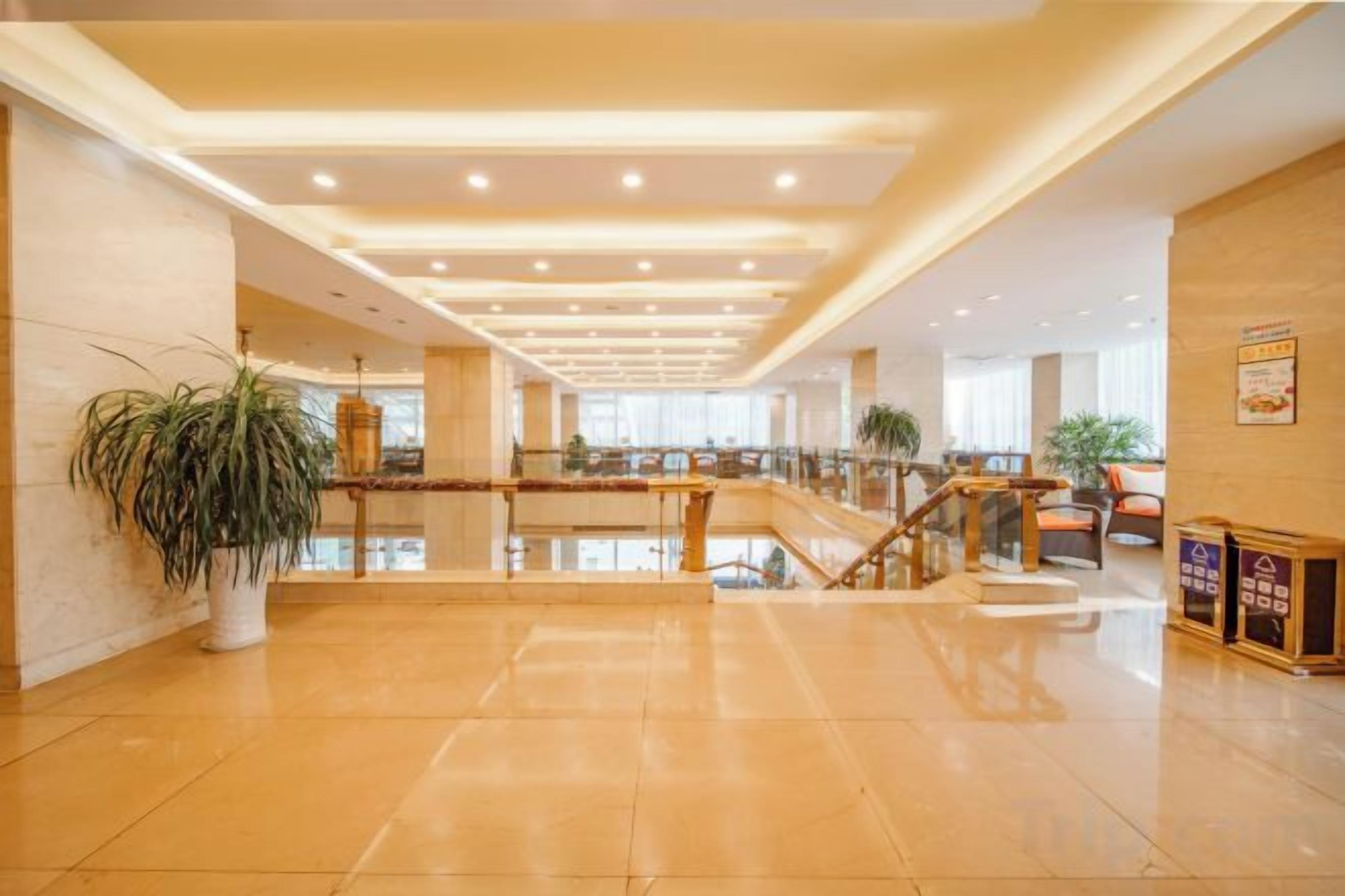 A spacious lobby with a central staircase, potted plants, and a polished floor.