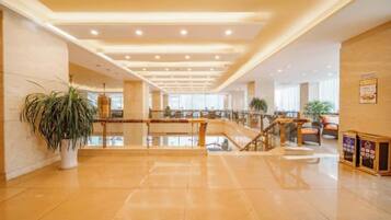 A spacious lobby with a central staircase, potted plants, and a polished floor.
