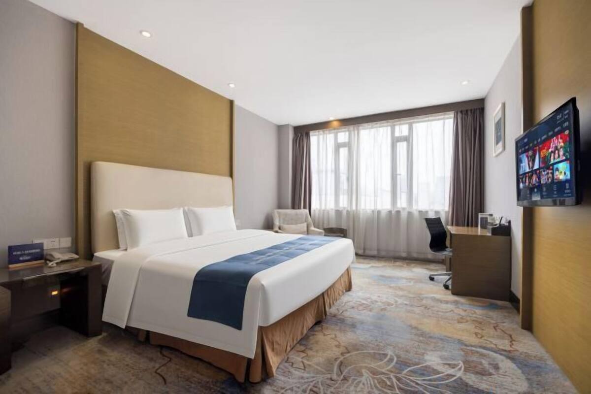 Une chambre d’hôtel avec un grand lit, un bureau, une chaise et un téléviseur fixé au mur.