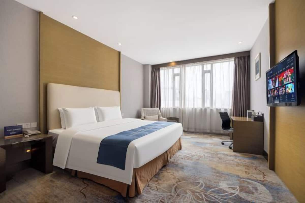 A hotel room with a large bed, a desk, a chair, and a television mounted on the wall.