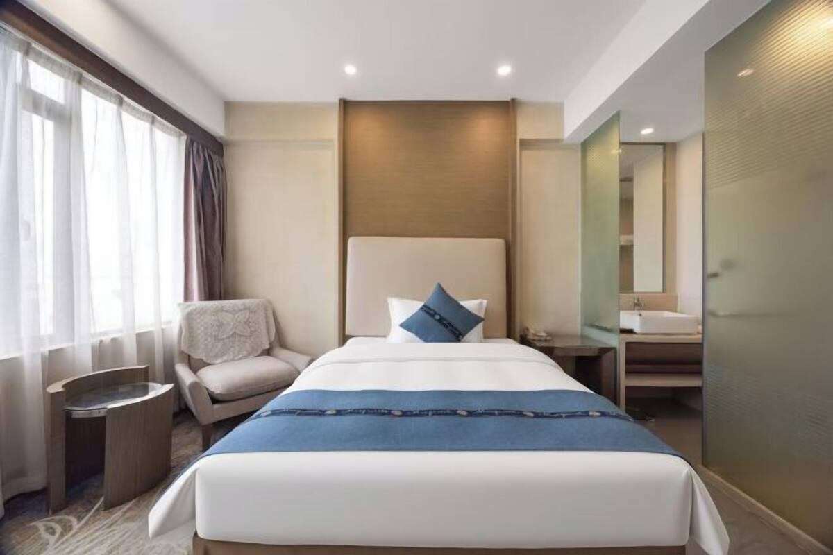 Une chambre d’hôtel avec un grand lit, une chaise, une table de chevet, un miroir et une salle de bain équipée d’un lavabo et d’un miroir.
