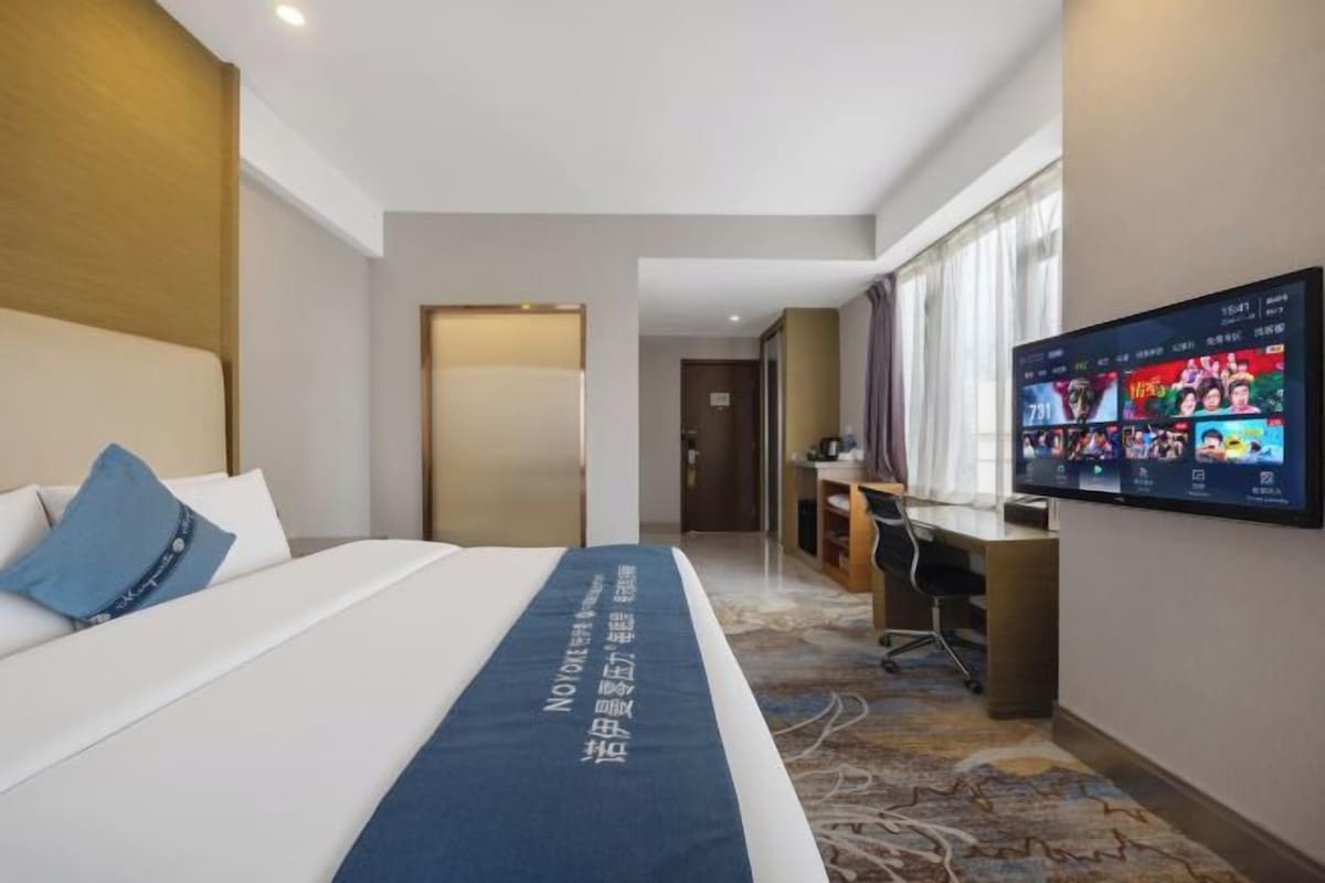 Habitación de hotel con cama, escritorio, televisor y piso alfombrado.