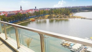 Blick auf ein Flussufer mit Glasgeländer, eine Anlegestelle mit Booten und Gebäude mit roten Dächern im Hintergrund.