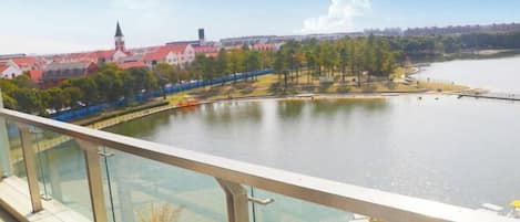 A riverside view with a glass railing, a dock with boats, and buildings with red roofs in the background.