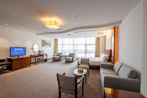 Ein Hotelzimmer mit Fernseher, Sitzgelegenheit und großen Fenstern.