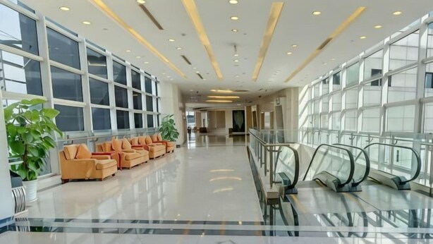 Eine geräumige Lobby mit einer langen Korridor, einer Sitzecke mit orangefarbenen Stühlen und einer Glaswand.