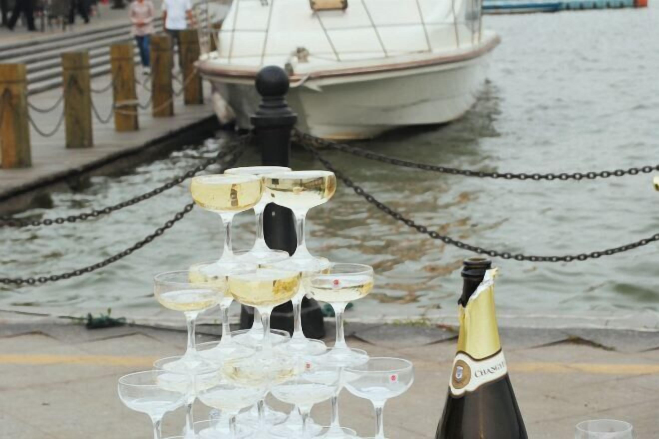 A champagne bottle and glasses on a dock by a body of water.