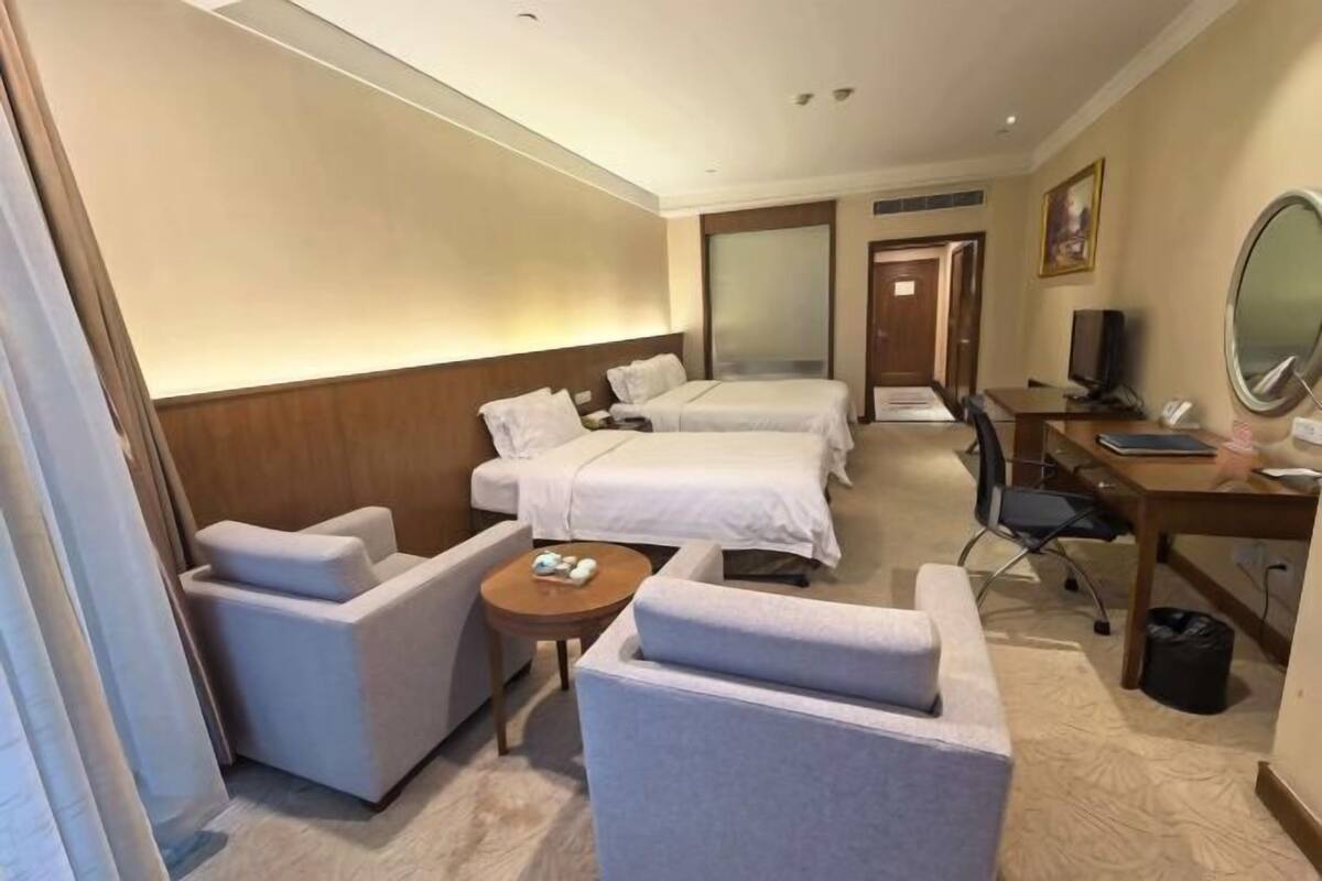 Habitación de hotel con dos camas, un escritorio, una silla, una mesita y un televisor.