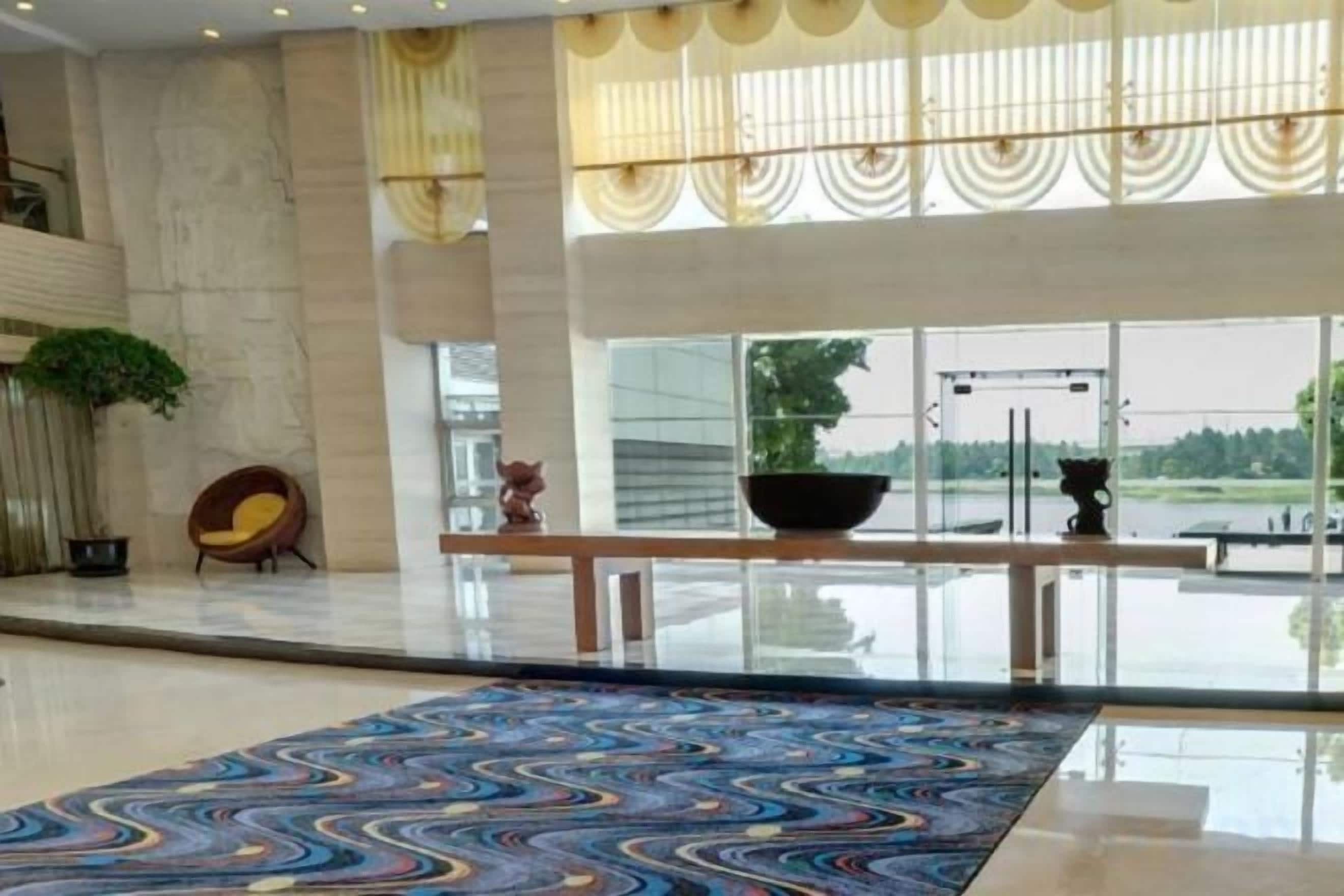 A spacious lobby with a large patterned carpet, a seating area with a chair, and a view of a body of water through large windows.