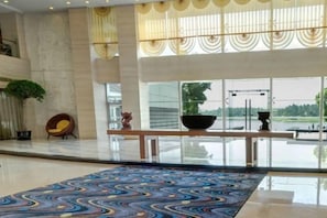 A spacious lobby with a large patterned carpet, a seating area with a chair, and a view of a body of water through large windows.