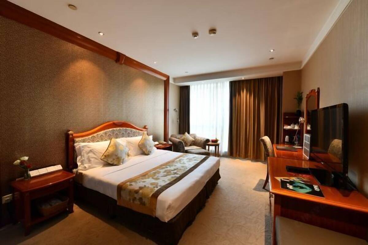 Habitación de hotel con una cama grande, un escritorio con computadora, televisor y ventana con cortinas.